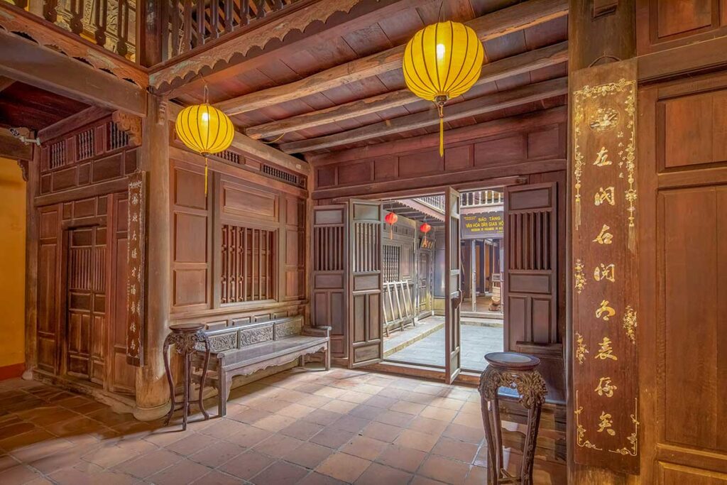 Interior hallway of the Museum of Folk Culture in Hoi An, carved wooden architecture lit by yellow lanterns leading to the central courtyard