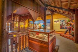 “Performing-arts gallery at the Hoi An Folklore museum featuring festival dioramas, a lion dance figure, and glass cases of traditional instruments.