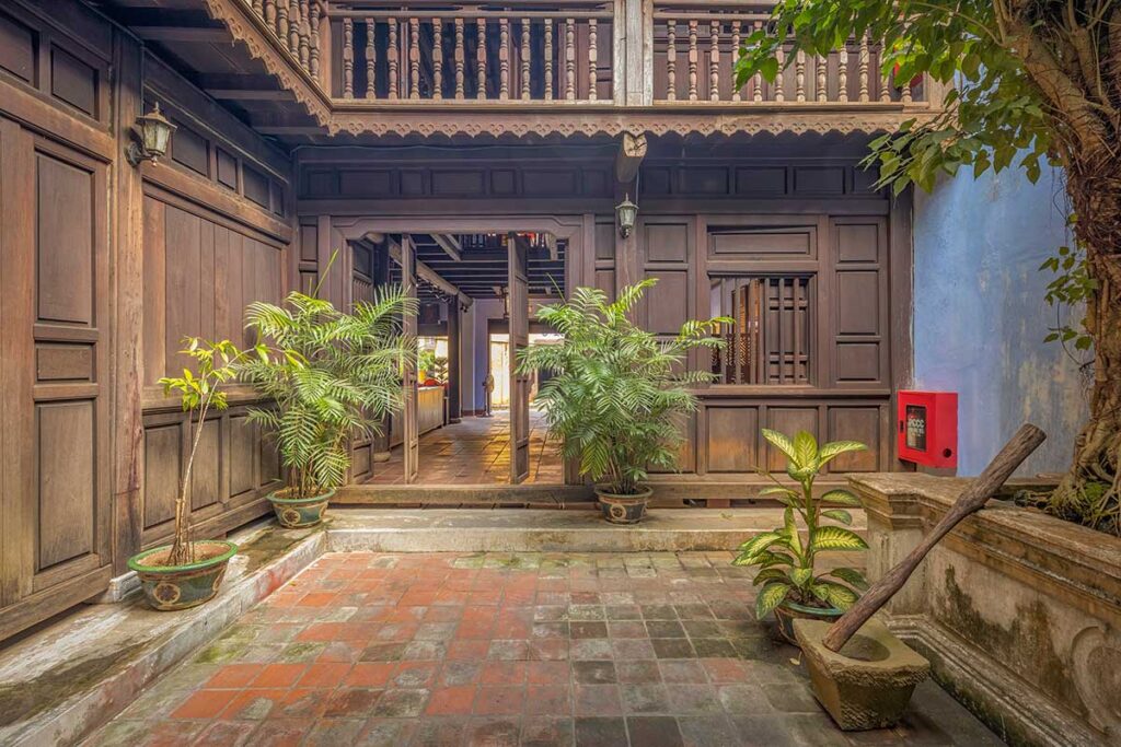 Courtyard of the Museum of Traditional Medicine in Hoi An with potted plants, wooden architecture, and an old wooden mortar and pestle