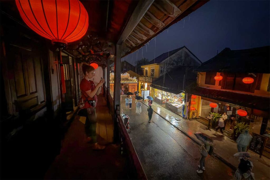Balcony view from Phung Hung Old House at night with glowing red lanterns overlooking the lantern-lit streets of Hoi An in the rain.