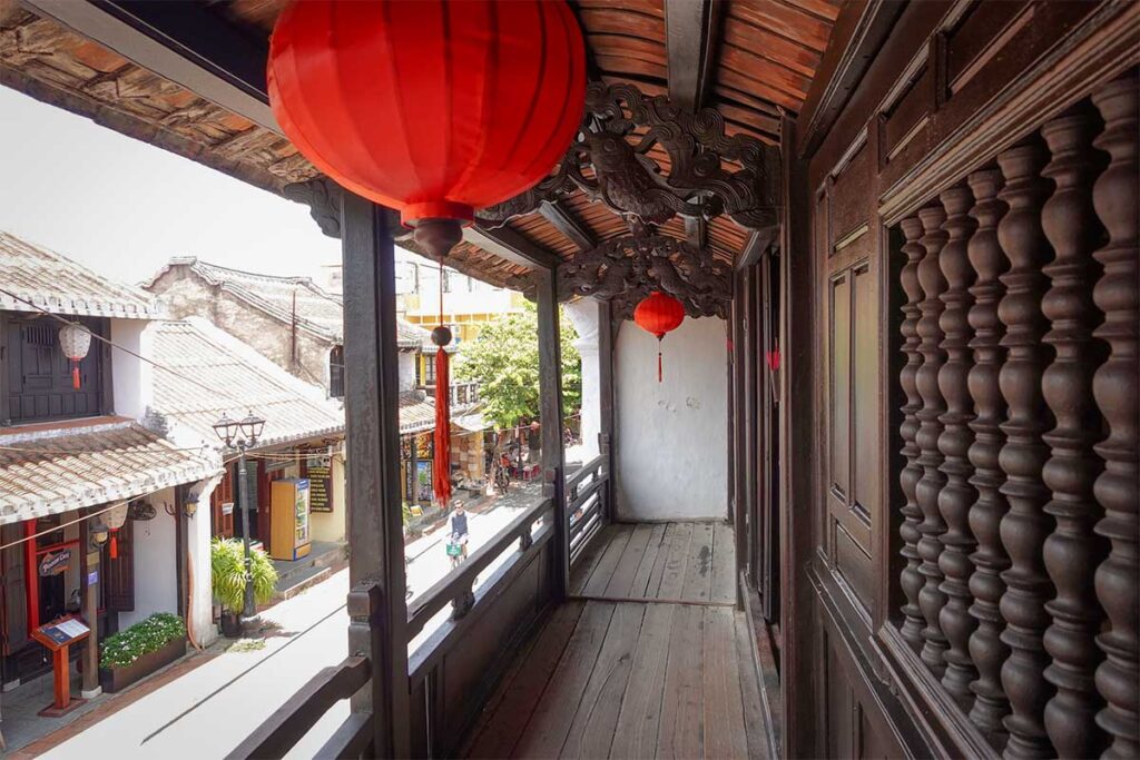 Second floor of Phung Hung Old House in Hoi An featuring wooden beams, worship area, and display cabinets with old ceramics and artifacts.