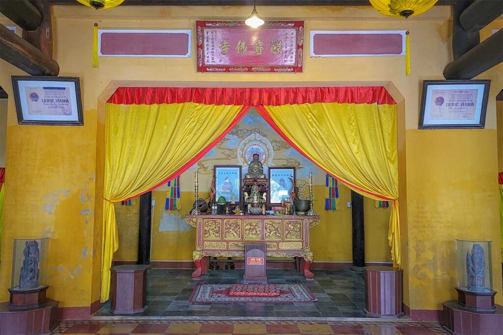 Buddhist altar with golden statue and yellow curtains inside Quan Am Pagoda Hoi An – ornate shrine showcasing traditional Vietnamese temple decor.