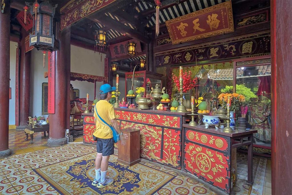 Tourist praying at richly decorated altar of Quan Cong Temple in Hoi An