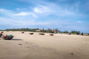 Wide sandy stretch of Tam Thanh Beach with basket boats dotting the shoreline, offering a glimpse into authentic fishing culture near Hoi An.