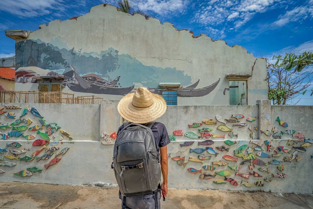 Tourist admiring a creative fish-themed mural installation in Tam Thanh Mural Village, central Vietnam.