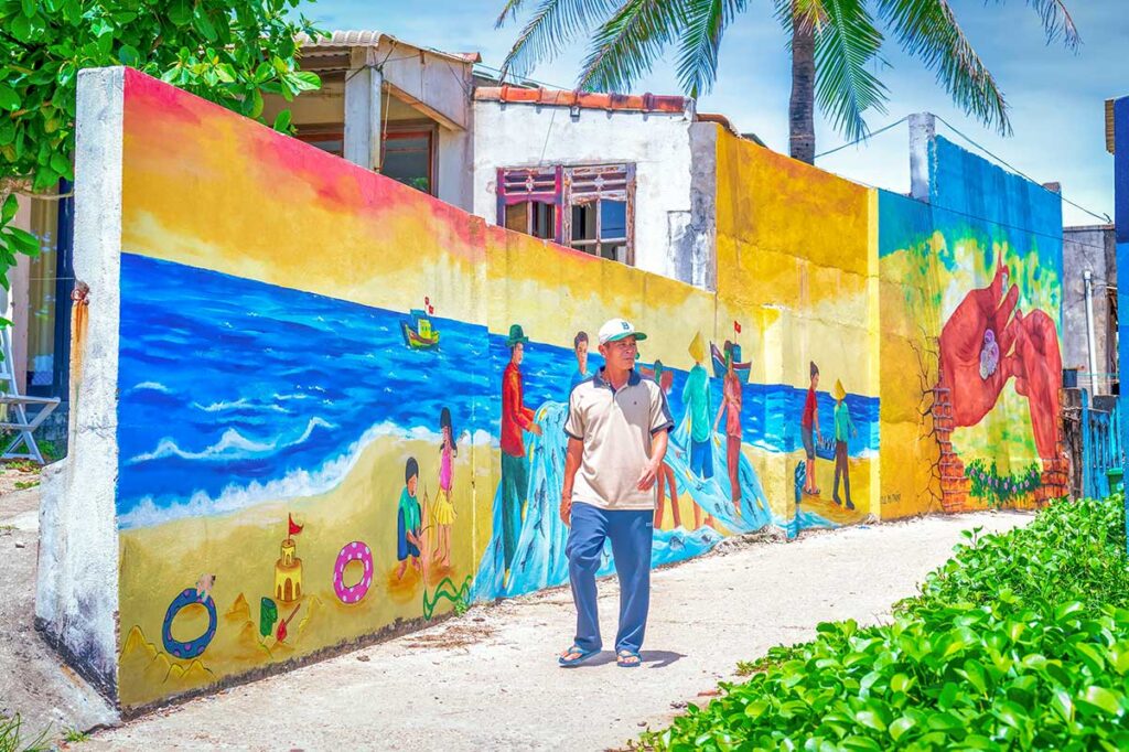 Colorful seaside mural in Tam Thanh Mural Village with a young girl’s portrait overlooking the ocean, blending art with village life.
