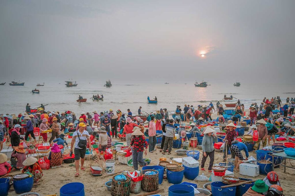 Large crowd trading seafood at Tam Tien Fish Market during sunrise.