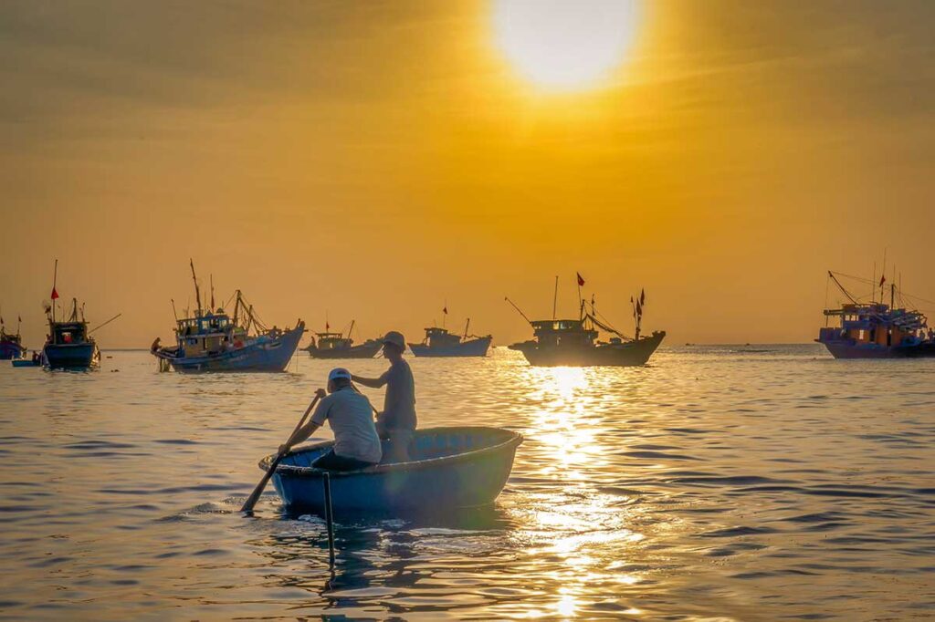 Sunrise at Tam Tien Fish Market with fishing boats and basket boats returning to shore.