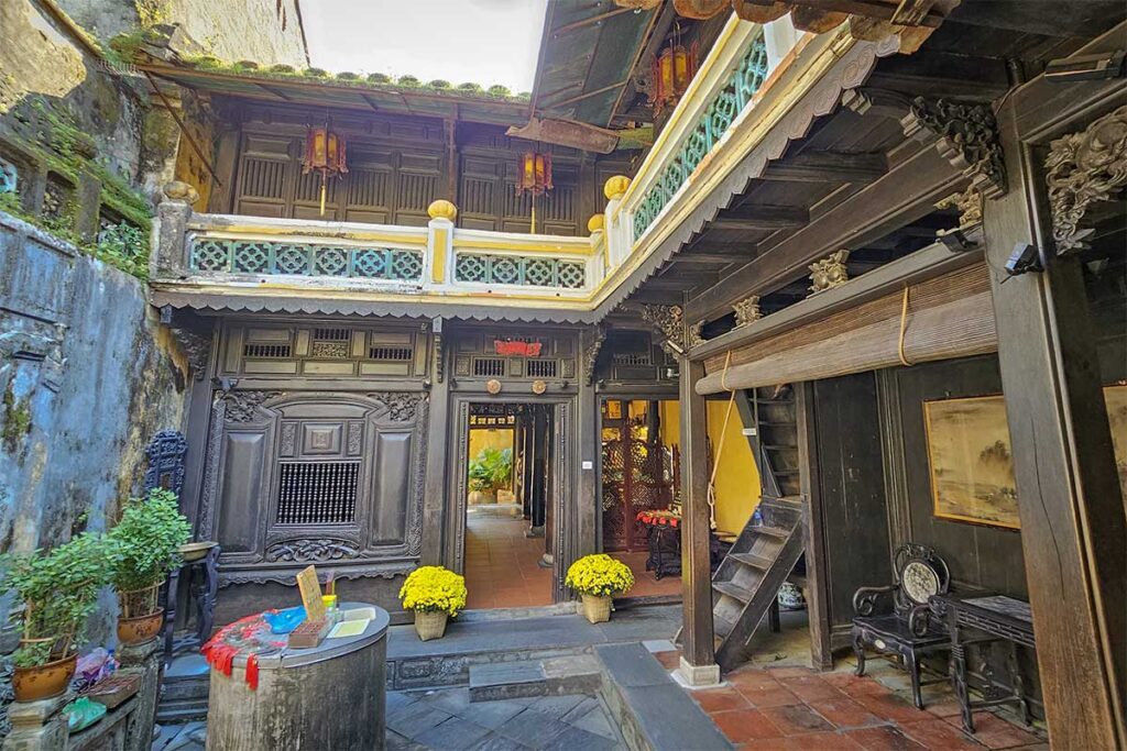 Courtyard of Tan Ky Old House in Hoi An, with carved wooden balcony, yellow walls, potted chrysanthemums, and a heritage water jar