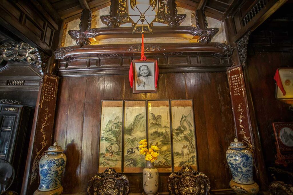 Ancestral altar inside Tan Ky Old House, with carved wooden details, ceramic vases, and a family portrait above traditional paintings