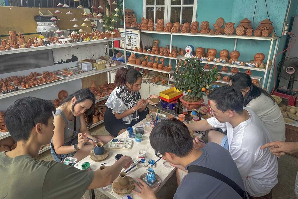 Painting workshop at Thanh Ha Pottery Village Hoi An – Tourists painting small clay vases as part of a hands-on pottery experience.