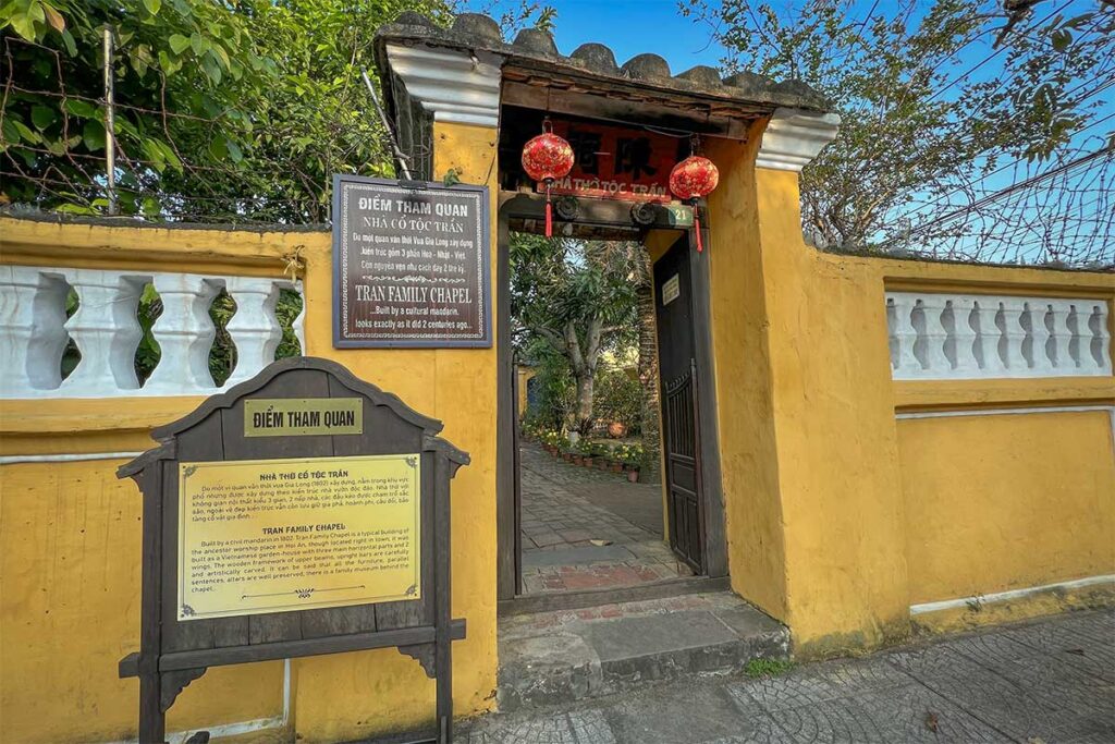 Entrance courtyard of Tran Family Chapel in Hoi An, with potted flowers and traditional yellow walls leading to the ancestral house.