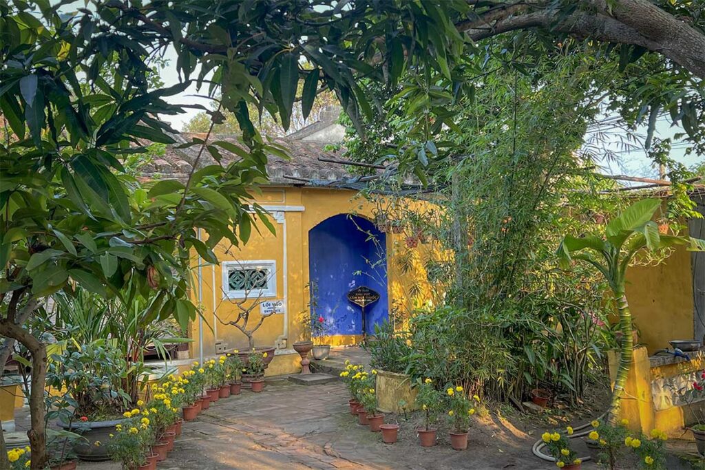 Courtyard garden of Tran Family Chapel in Hoi An with flowering plants, shaded trees, and historic architecture.