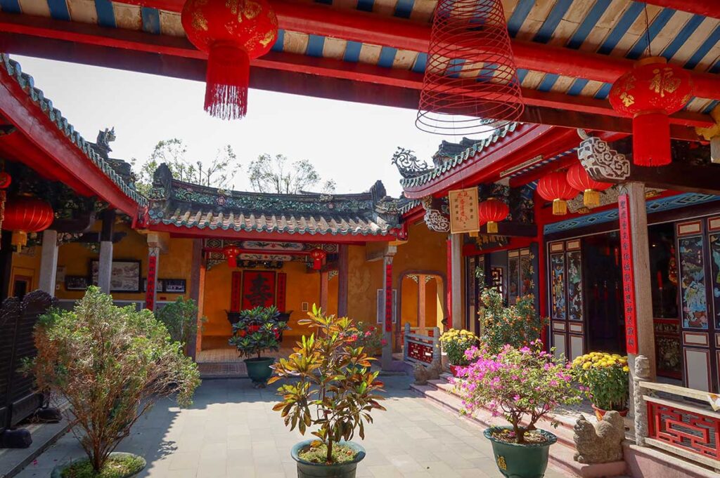 Courtyard of Trieu Chau Assembly Hall in Hoi An Vietnam – Open courtyard with potted plants, red lanterns, and traditional tiled roofs decorated with colorful dragons.