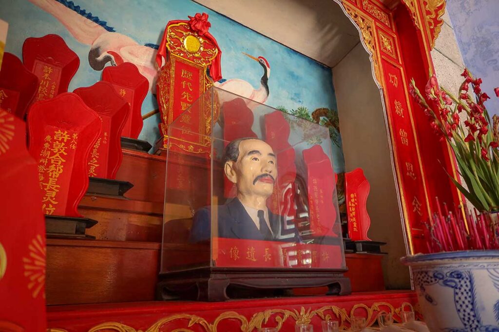 Ancestor shrine at Trieu Chau Assembly Hall in Hoi An – Red altar with portrait bust, incense offerings, and calligraphy tablets honoring past leaders of the Chinese community.