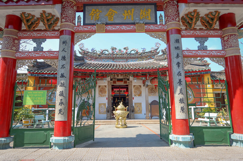 Trieu Chau Assembly Hall in Hoi An Old Town, featuring red pillars, ornate carvings, and a traditional Chinese gate with intricate roof decorations.