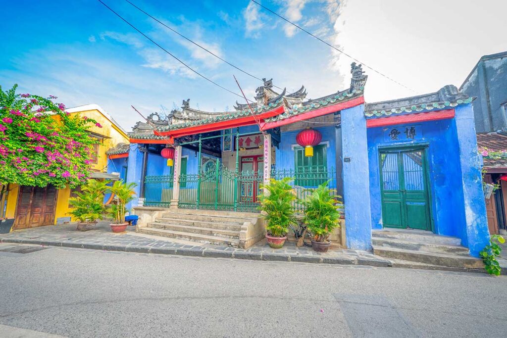 Street view of Trung Hoa Assembly Hall in Hoi An Ancient Town, vibrant blue walls and ornate tiled roof.