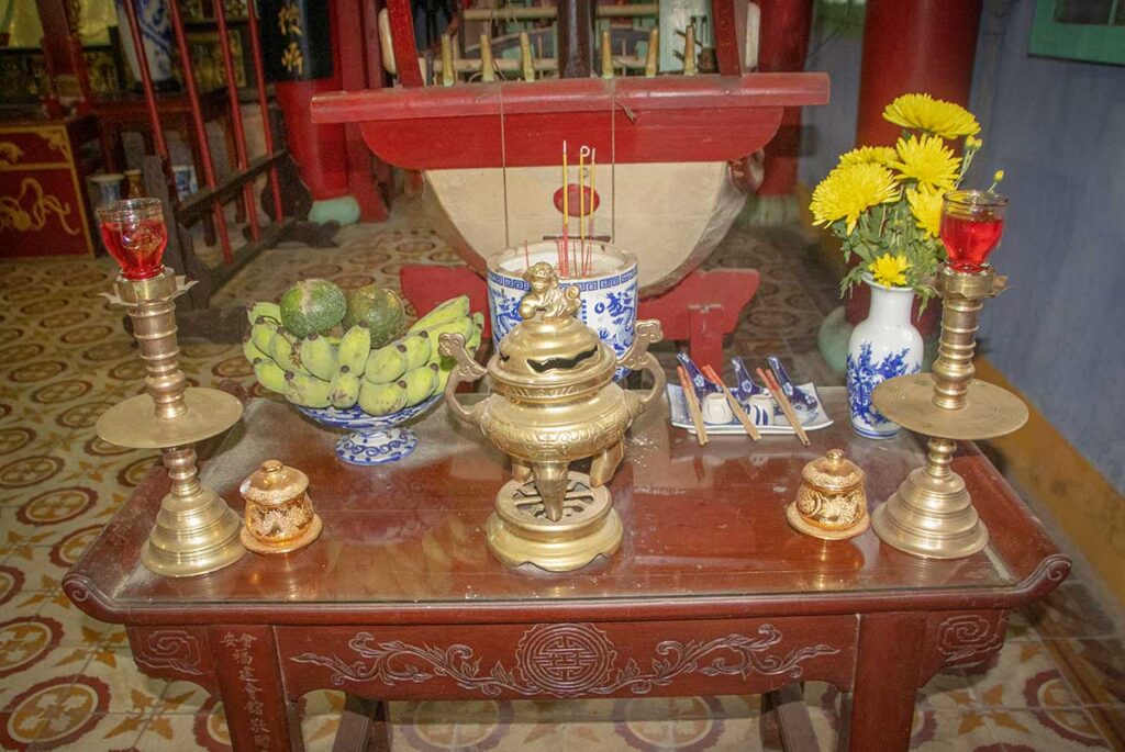 Altar table at Trung Hoa Assembly Hall in Hoi An, set with incense burners, candles, and fruit offering