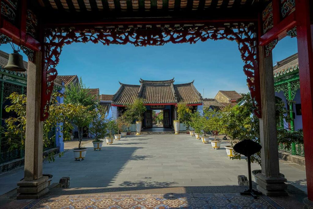 Courtyard of Trung Hoa Assembly Hall in Hoi An, with traditional tiled roof buildings framed by carved wooden gates.