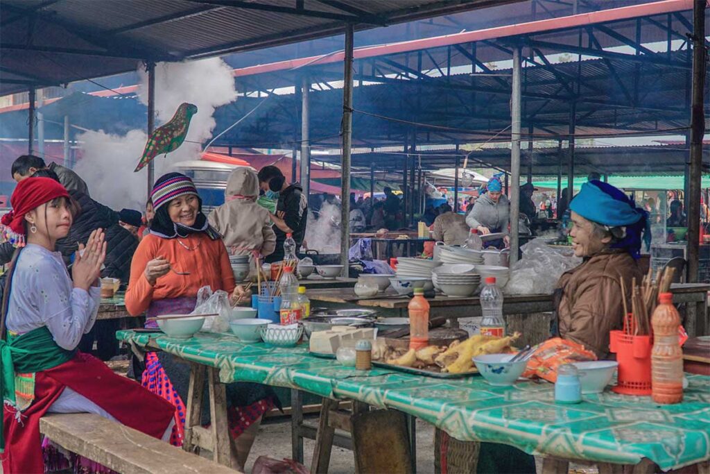 Local ethnic minorities sitting at a table eating street food dishes at the Dong Van Market