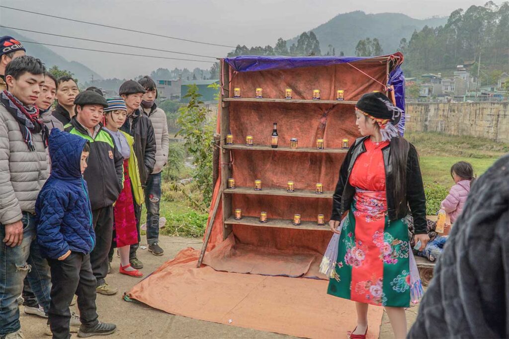 A game to throw balls at bottles in a closet hosted by an ethnic woman at Dong Van Market