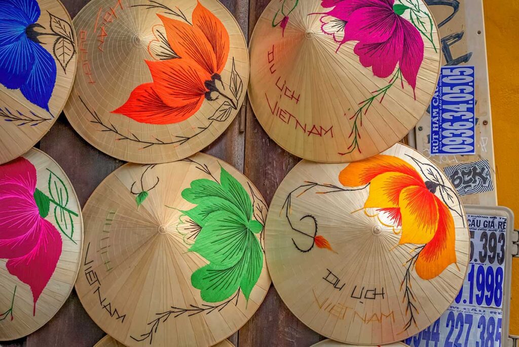 Decorated Vietnamese conical hats (nón lá) with hand-painted floral designs for sale in a Hoi An souvenir shop — a traditional gift with a local touch