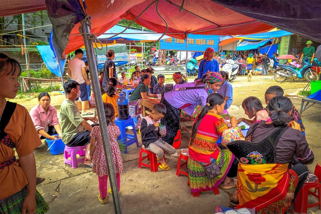 Colorful local ethnic people sitting at a food stall eating freshly made dishes at the Lung Khau Nhin Market