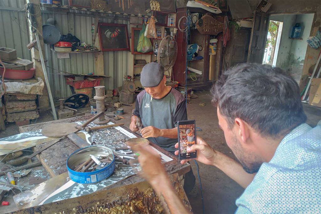 Visitor photographing an artisan handcrafting bronze items at Phuoc Kieu Bronze Casting Village, Hoi An.