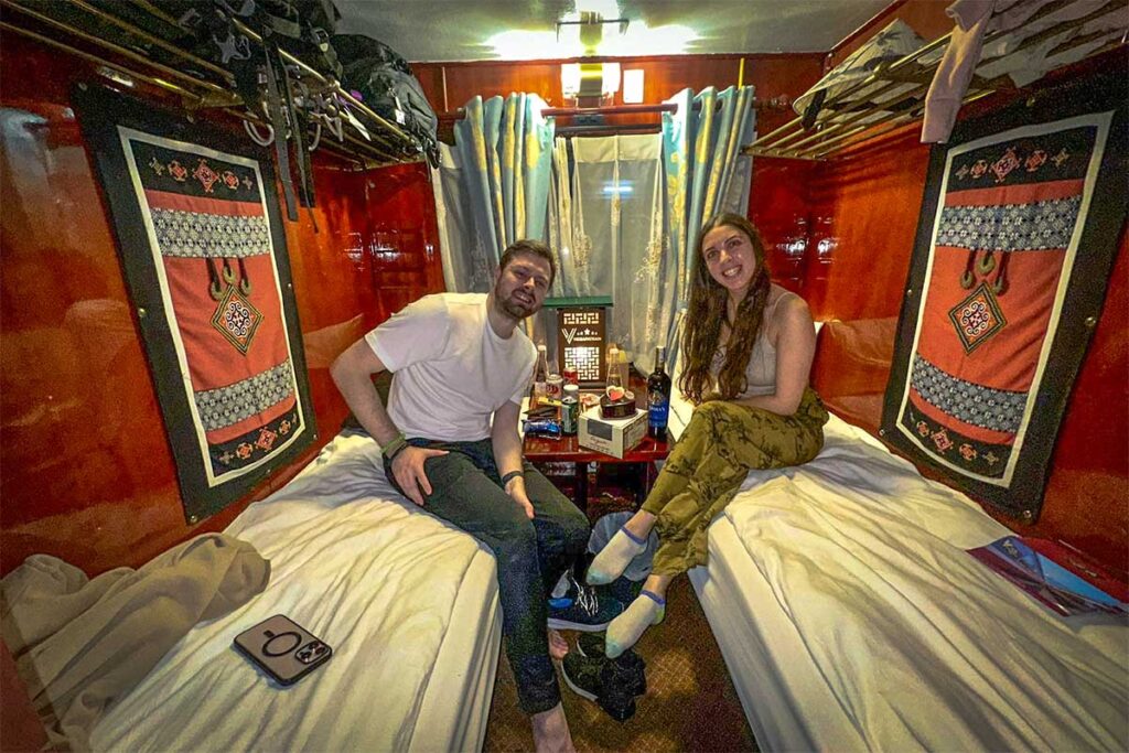 A couple sitting on twin beds inside a tourist train of VIC Sapa Train driving from Hanoi to Sapa