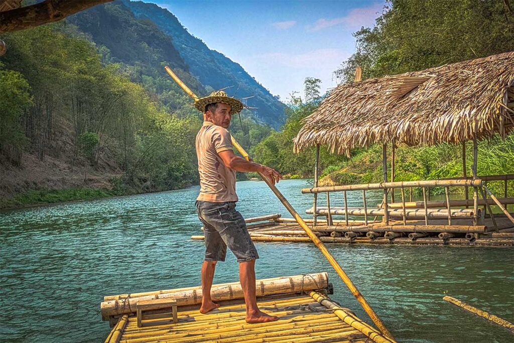 A local man using a stick to move a bamboo raft in Pu Luong through a stream