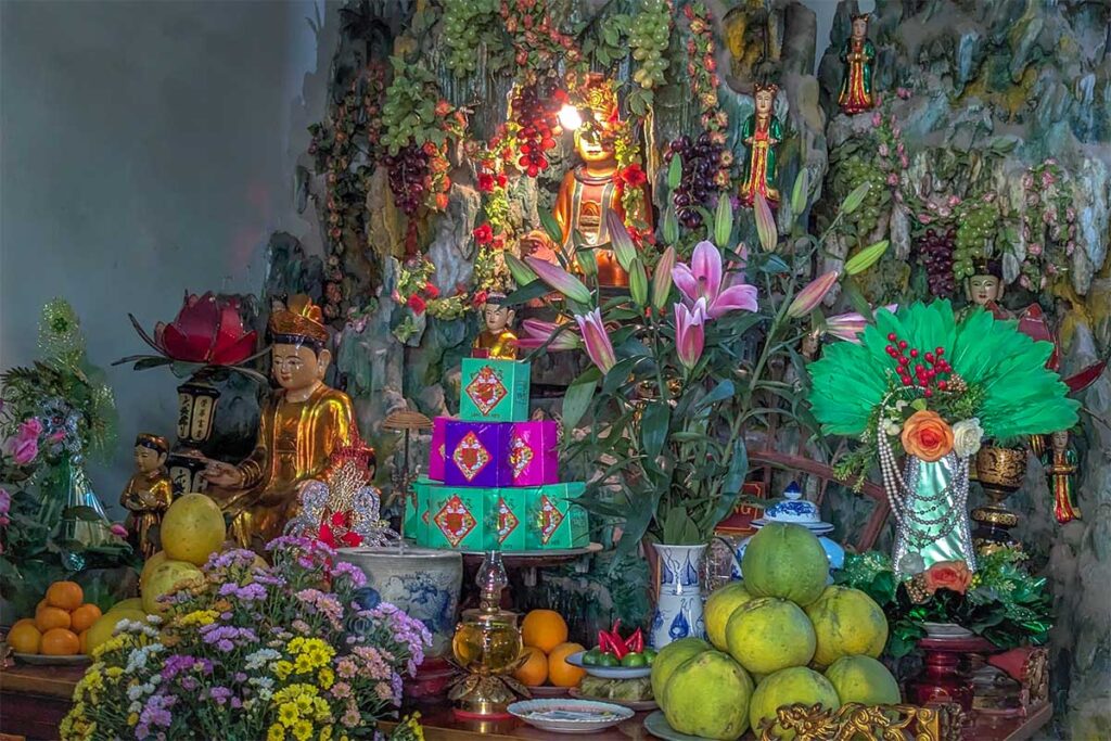 Seated statue of Đức Ông inside a rocky shrine at Boc Pagoda in Hanoi, believed to represent King Quang Trung, with smaller attendant figures and a small altar in front