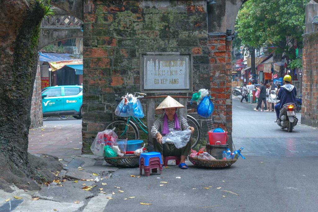 A woman selling street food right in front of Hanoi Old City Gate