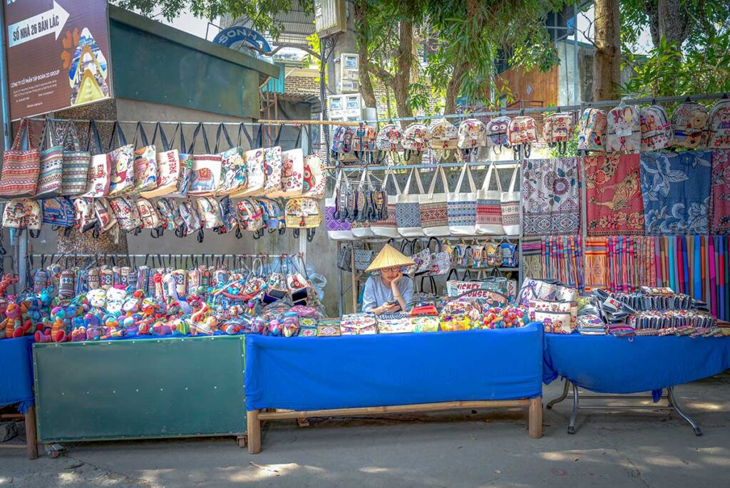 A girl with conical hat is sitting a souvenir stall selling locally made products in Lac Village