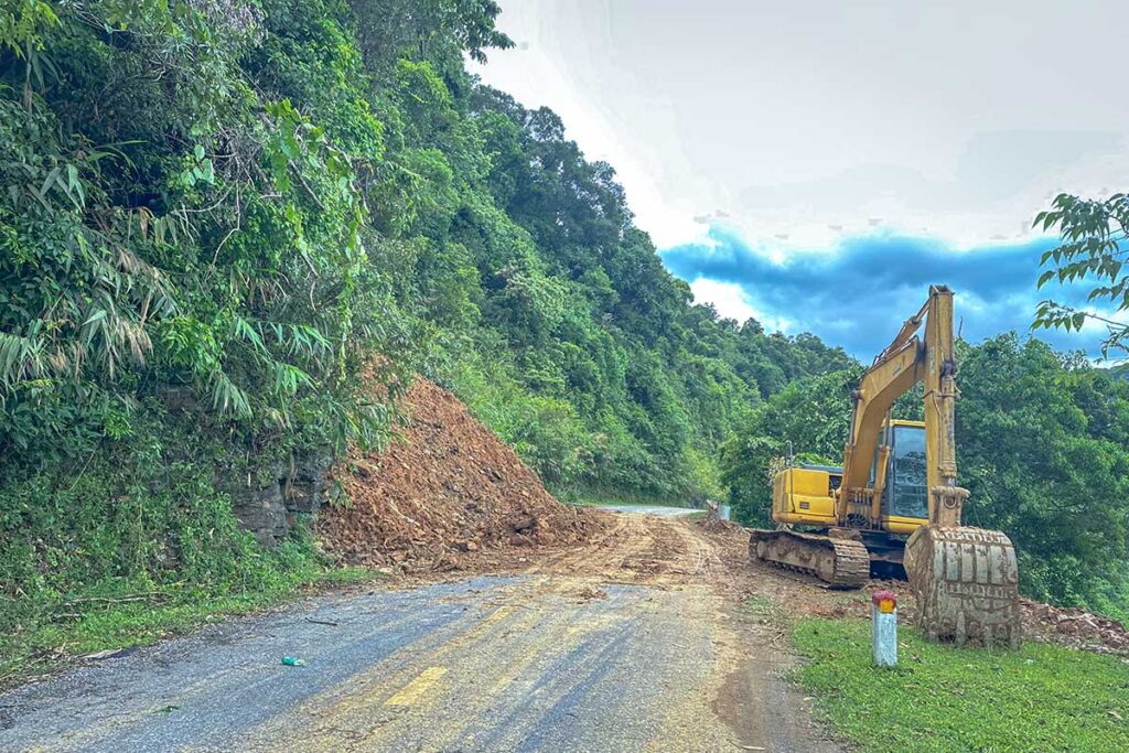 An excavator clearing a landslide from a mountain road in Vietnam