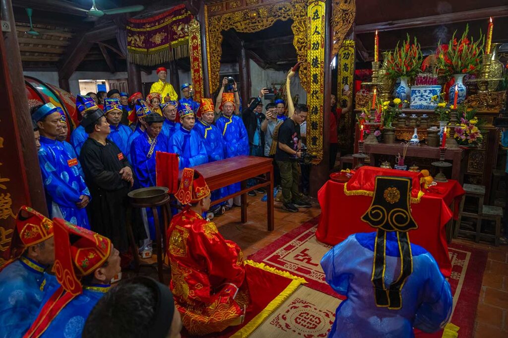 People wearing traditional clothes in red and blue are sitting inside a temple doing a ritual for Lim Festival