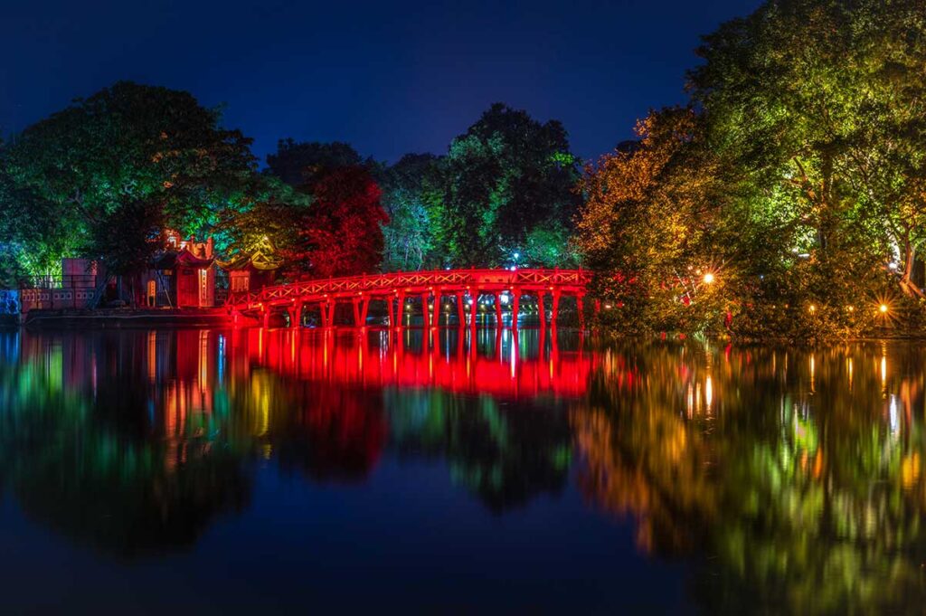 The The Huc Bridge seen in the evening with lights on the bridge reflecting in the water of Hoan Kiem Lake