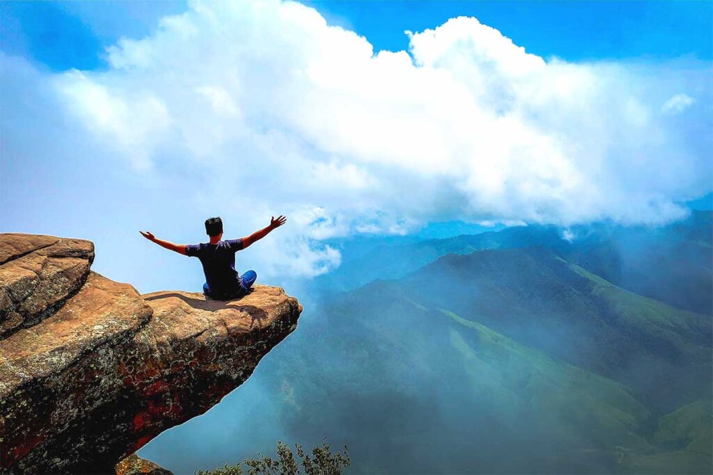 A man sitting on a rock  that sticks out so it looks a very dangerous place to sit