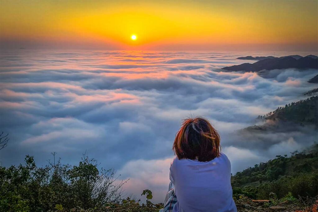 A girl sitting on a mountain and watching a sea of clouds below here are Ta Xua, during a trekking in the nature reserve