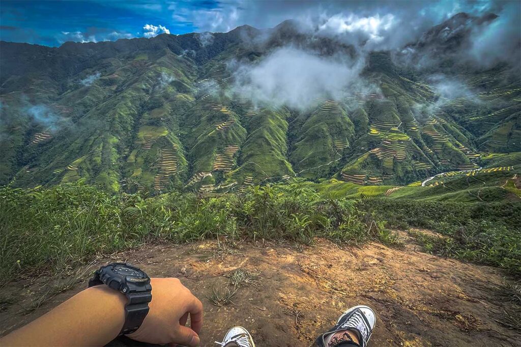 Two feet from a man sitting down with views of the mountain of Ta Xua during a trekking