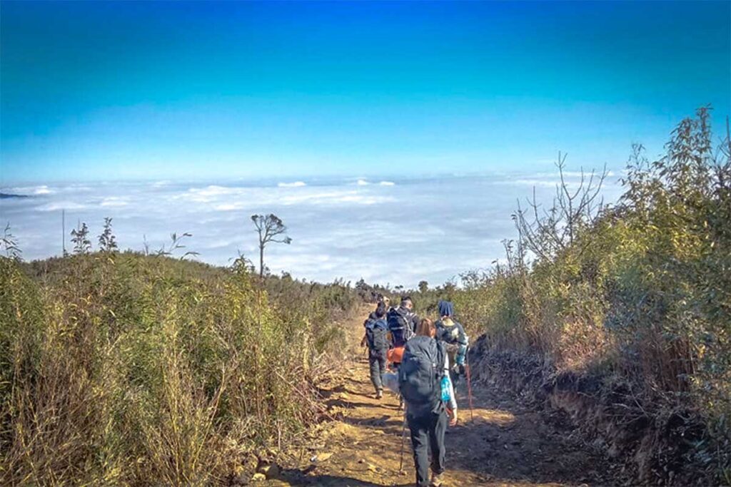 A group of travellers trekking in Ta Xua over a dirt path with on the background below them a sea of clouds