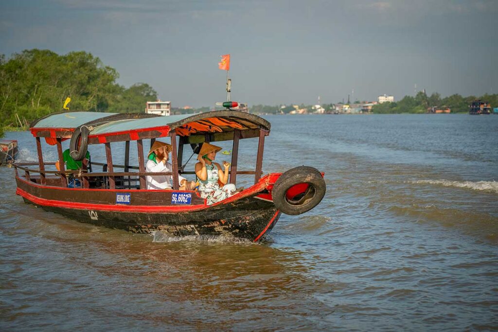 Tourist boat ride in Cai Be, Vietnam – travelers exploring the Mekong Delta canals by wooden boat.