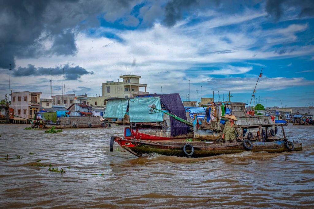 Boats on the Mekong River at Cai Be Floating Market under cloudy skies, showing daily river life in Tien Giang Province, Vietnam