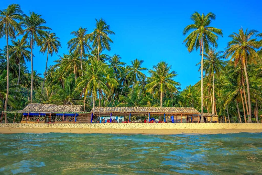 Cay Men Beach palm huts – Traditional palm-roof shelters by the beach with tall coconut trees, main swimming spot on Hon Lon.