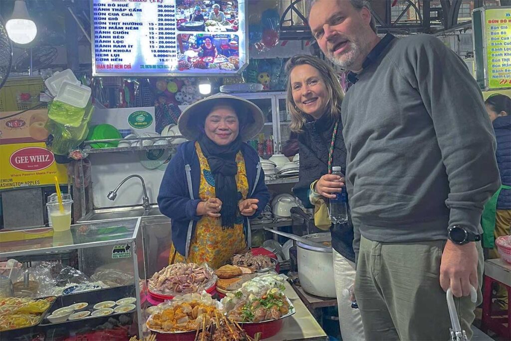 Two tourists posing for a photo at a local food vendor during a Hue Street Food Tour