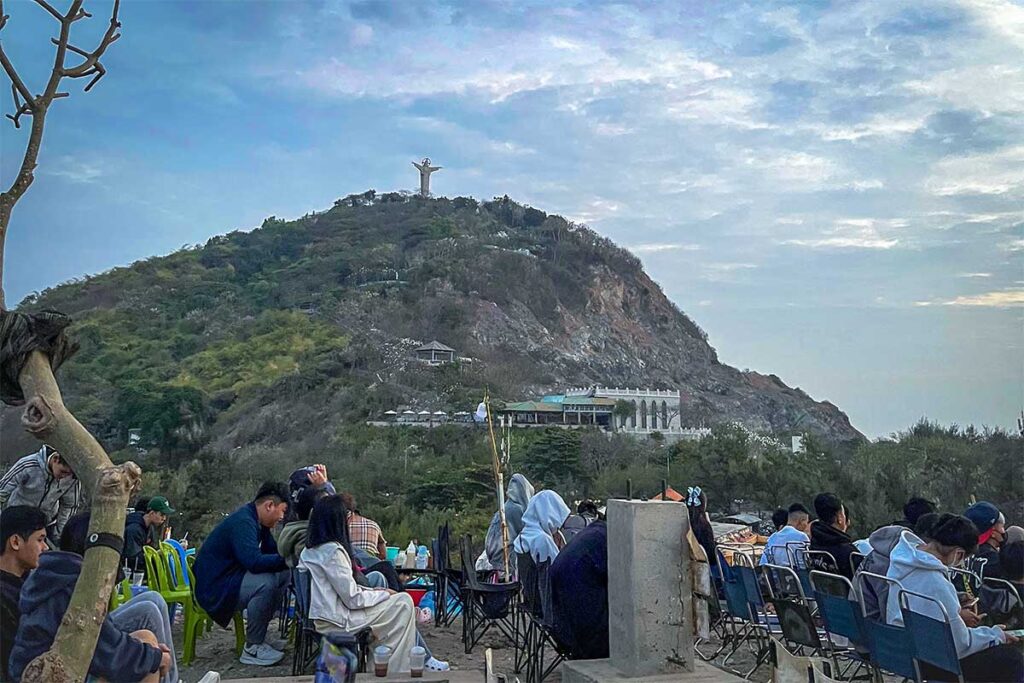People sitting on chairs at Nghinh Phong Cape with on the background Jesus Statue of Vung Tau on top of a hill