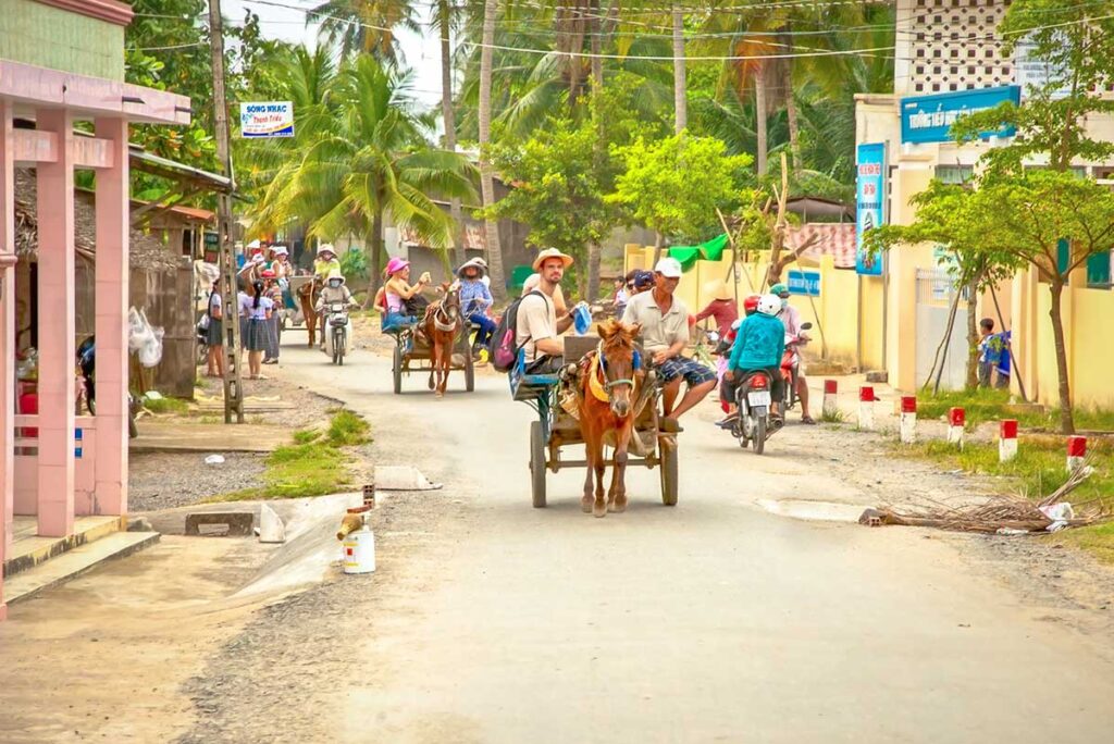 Tourists riding horse-drawn carts along a village road on Phoenix Island, Ben Tre, Vietnam.