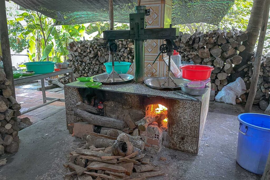 Traditional coconut candy workshop on Phoenix Island, Ben Tre, showing firewood stove and cooking pans used in candy-making demonstrations.