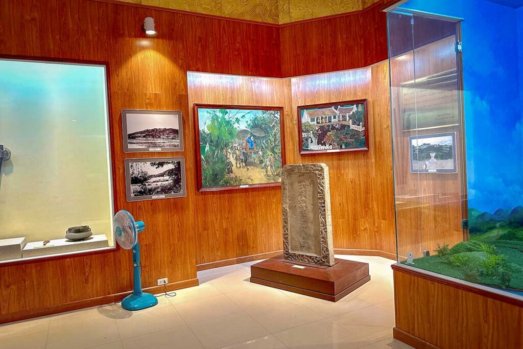 Exhibition hall inside Quang Trung Museum in Binh Dinh, displaying a stone stele alongside historic photographs and paintings about the Tay Son uprising.