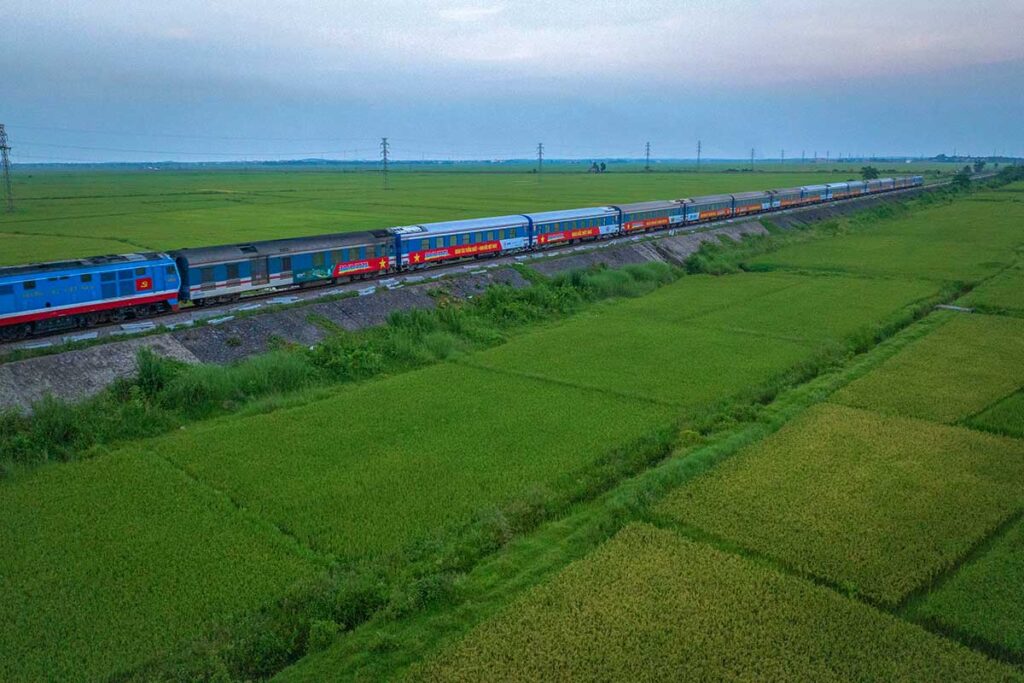 The Reunification Express Train of Vietnam rides through the countryside of Quang Binh with green rice fields