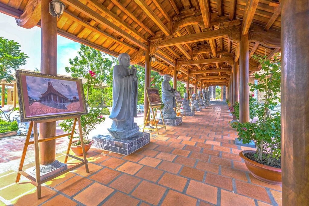 Corridor lined with stone Arhat statues and wooden pillars at Truc Lam Phuong Nam Zen Monastery in Can Tho.